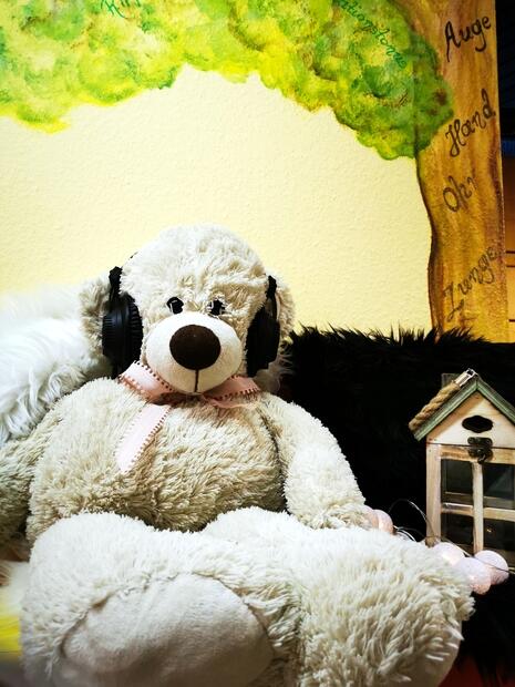 Ein Teddybär mit Kopfhörern sitzt auf einem Sofa.
